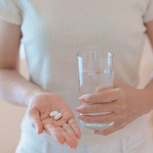 a person holding 2 tablets and a glass of water