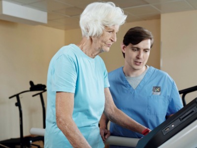 woman walking on treadmill under control of young male physiotherapist