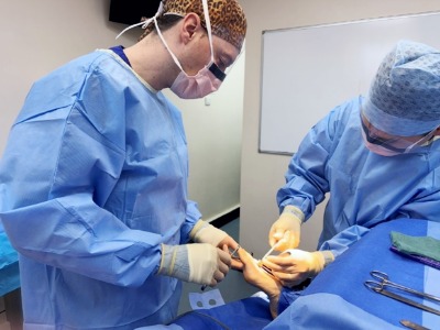 Scott with the foot surgeon in scrubs working on a foot